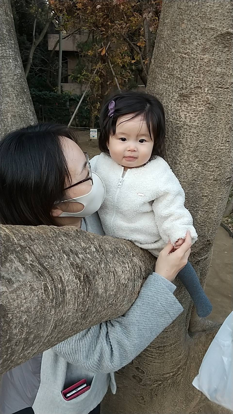 公園の木の枝に座っている赤ちゃんを支える母。