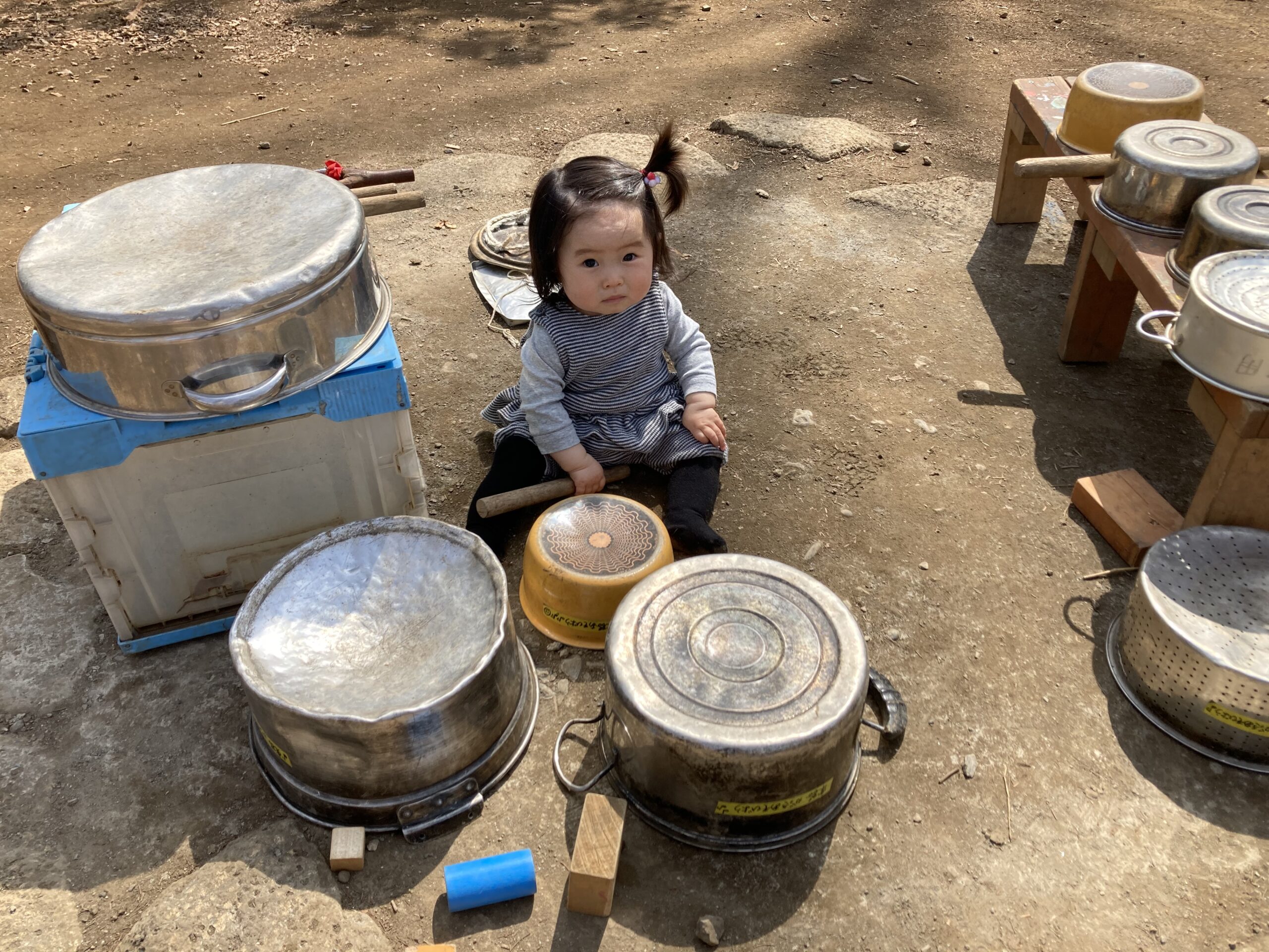 複数のお鍋の太鼓に囲まれた子どもがこちらを見ている。しながわ区民公園の冒険ひろばでの写真。