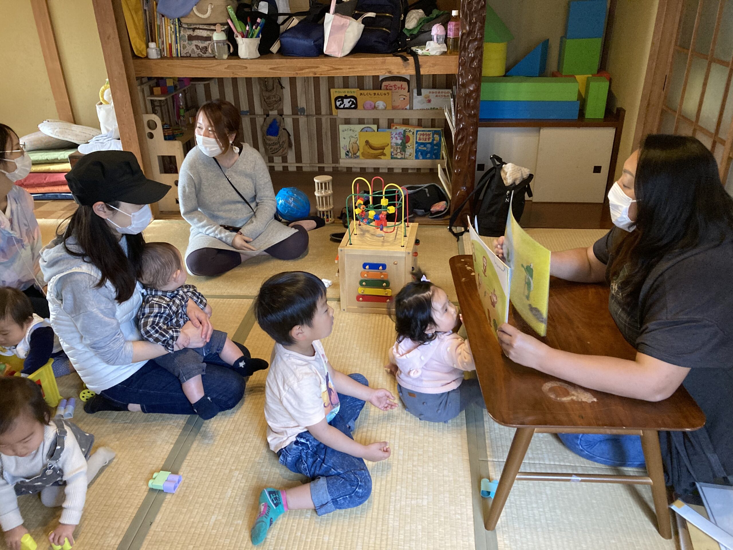 古民家の部屋で、子ども達が絵本の読み聞かせを真剣に見ている様子。品川区子育てひろば「つっくいた」