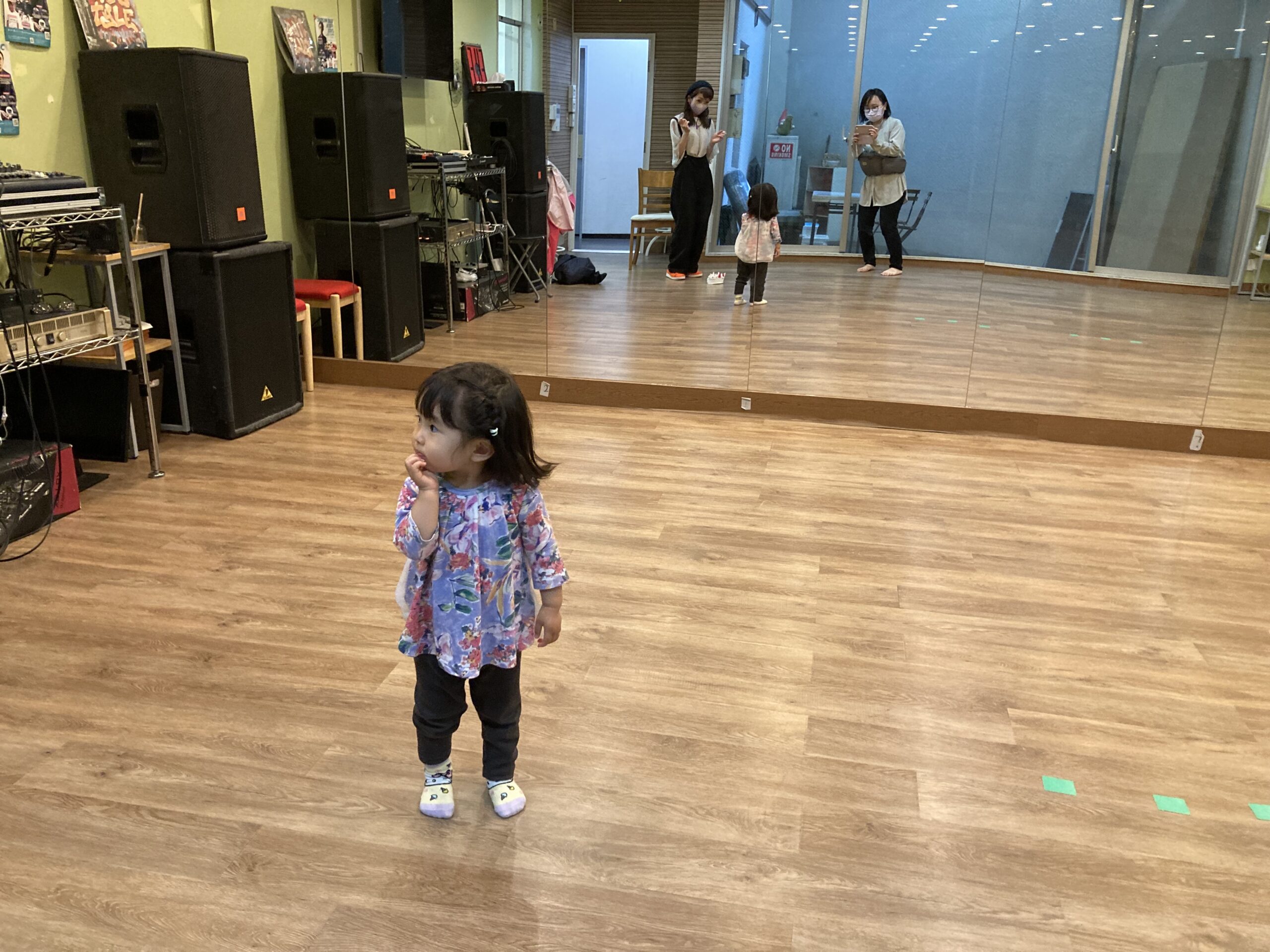 スタジオにいる2歳の女の子。横顔。鏡に大人が2人写っている。